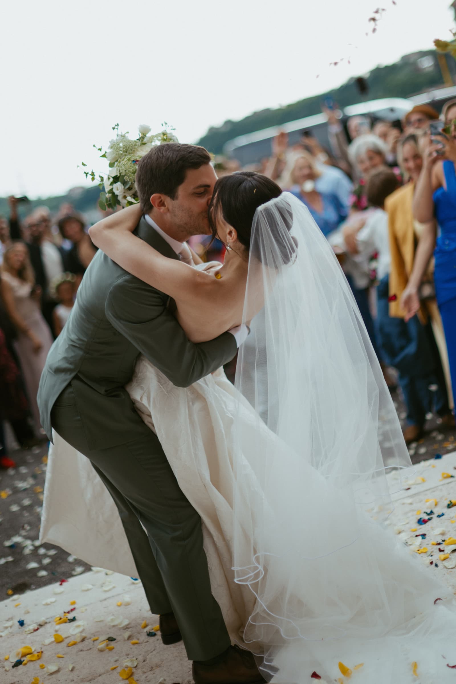 Bride and groom kissing as guests throw confetti, Italy