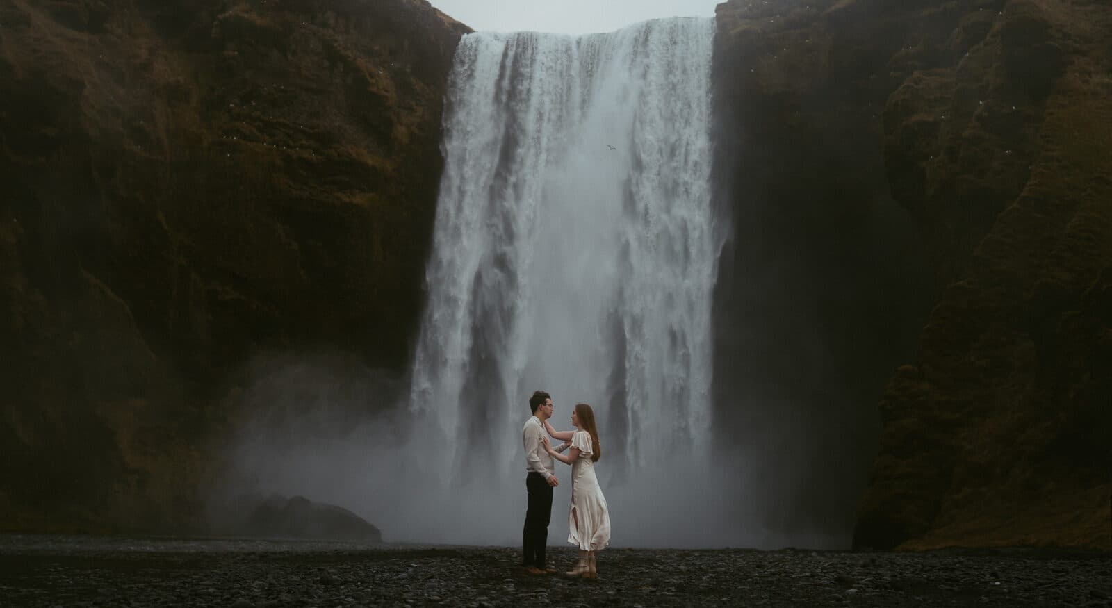 Couple standing in front of Skógafoss waterfall in Iceland on a misty day during their elopement