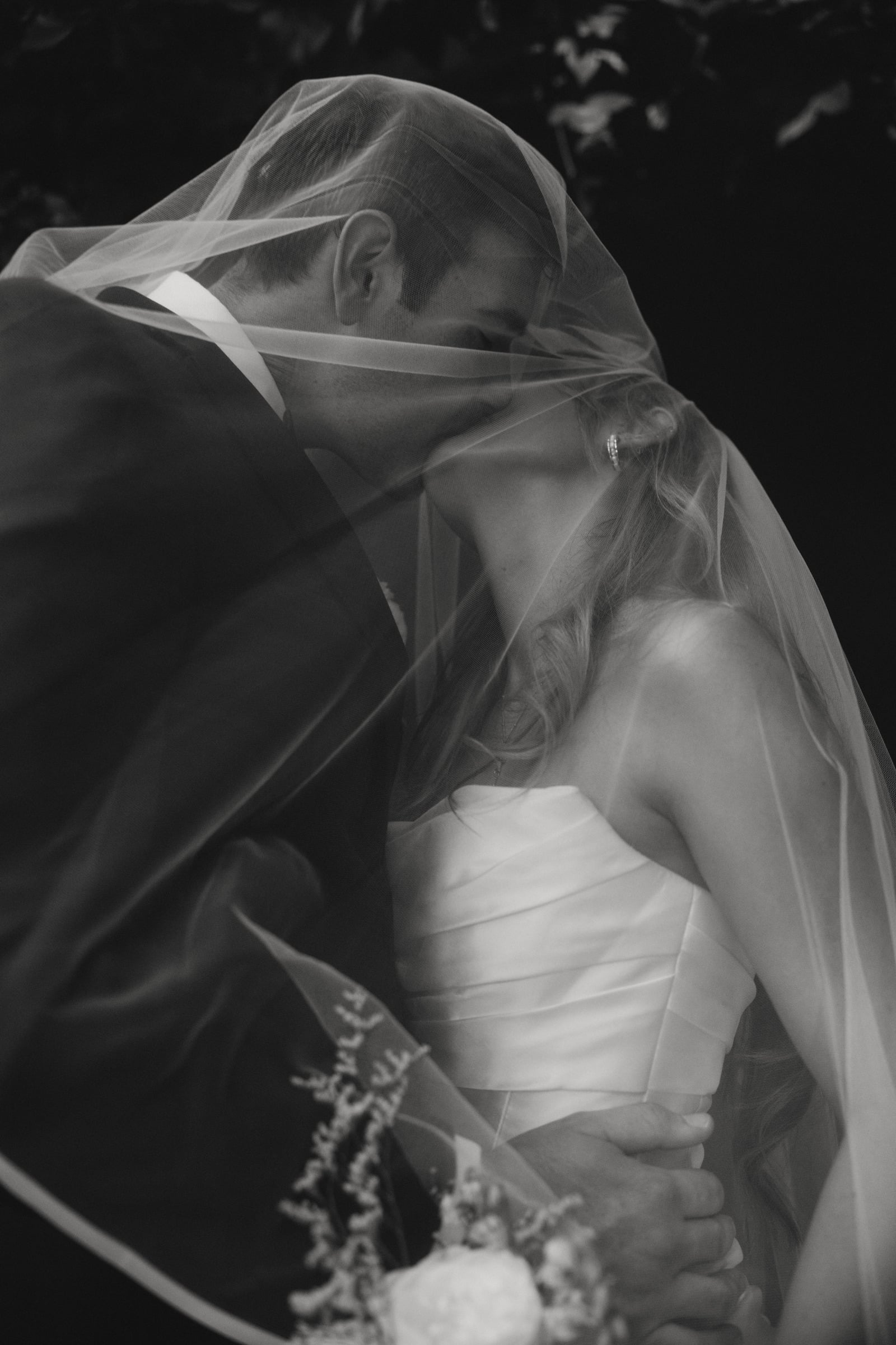 Bride and groom kissing under a veil, black and white, Italy