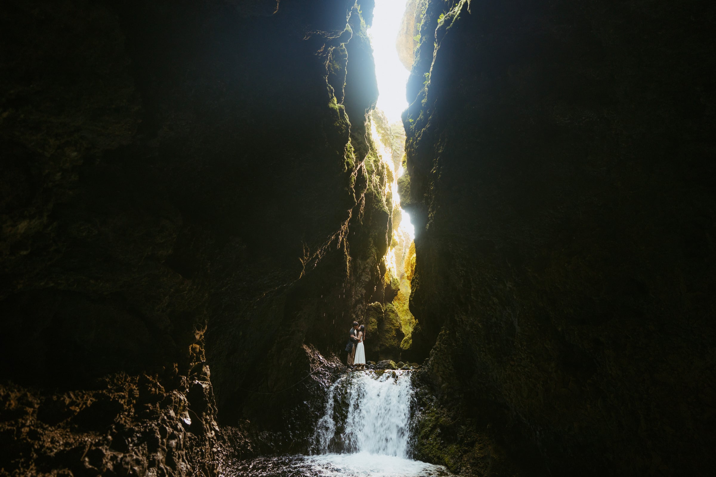 Couple standing in a shaft of light inside an Icelandic canyon