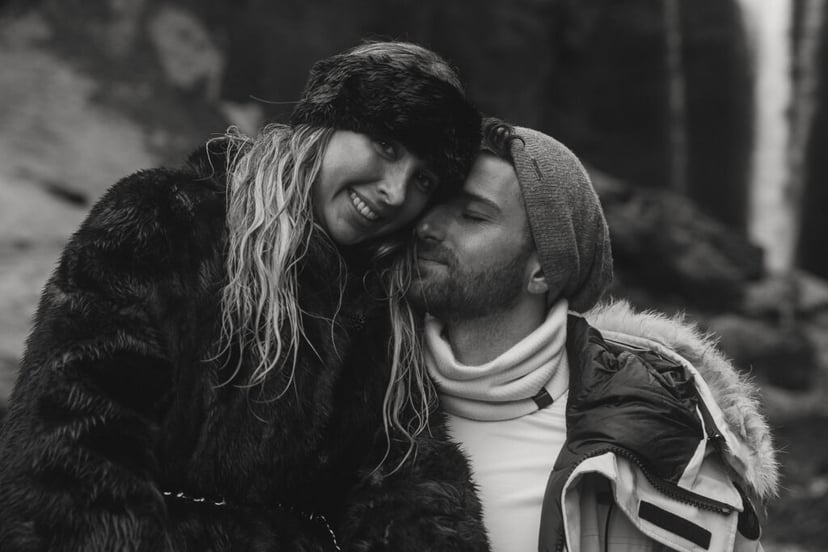 couple embracing in front of Skogafoss waterfall in Iceland after a surprise proposal. The dramatic Icelandic landscape, mist from the falls, and changing weather create a breathtaking backdrop for their engagement session.