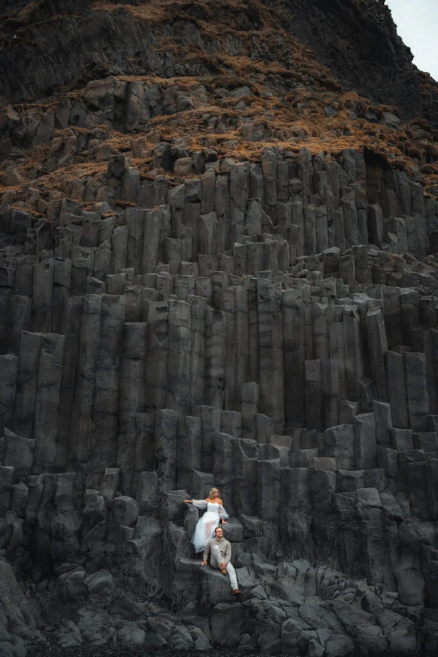 Couple sitting on the basalt columns at Reynisfjara black sand beach in Iceland