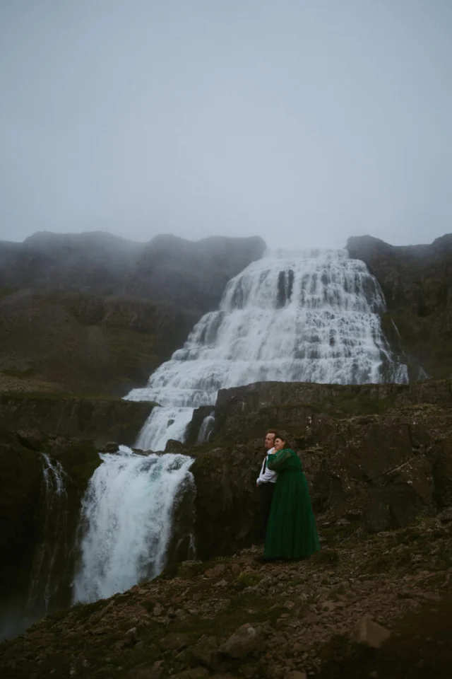 Couple embracing in front of the full cascade of Dynjandi waterfall on a foggy day in Iceland