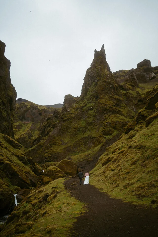 Couple walking along a dirt trail through the mossy canyon landscape of Þakgil in Iceland