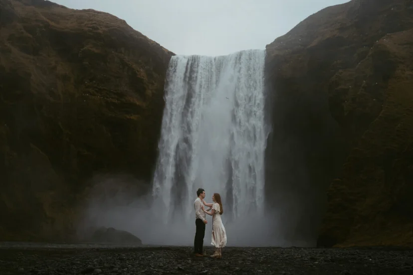 Couple embracing at the base of Skógafoss waterfall in Iceland with mist rising around them