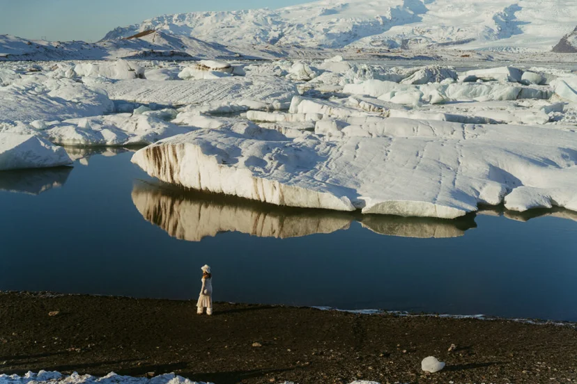 Person in a white dress standing near Jökulsárlón Glacier Lagoon with snow-covered mountains in the background