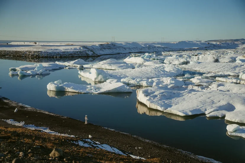 Person standing on the shoreline of Jökulsárlón Glacier Lagoon, surrounded by floating icebergs in winter