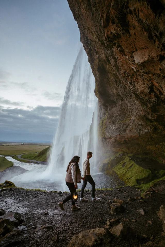 Couple walking behind Seljalandsfoss waterfall in Iceland during a cloudy summer day
