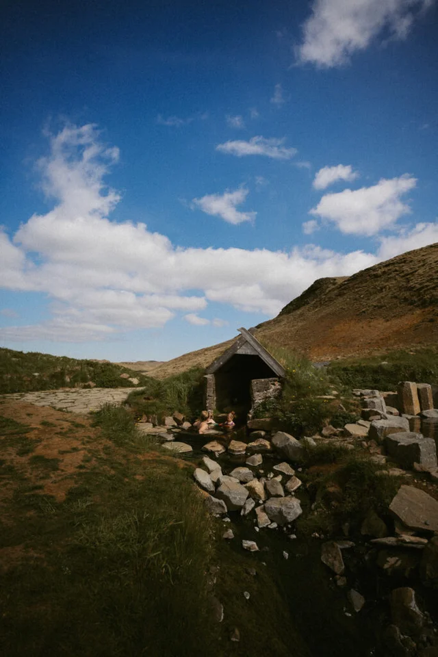 Wide view of Hrunalaug hot spring surrounded by grass and rocks with bathers enjoying the warm water