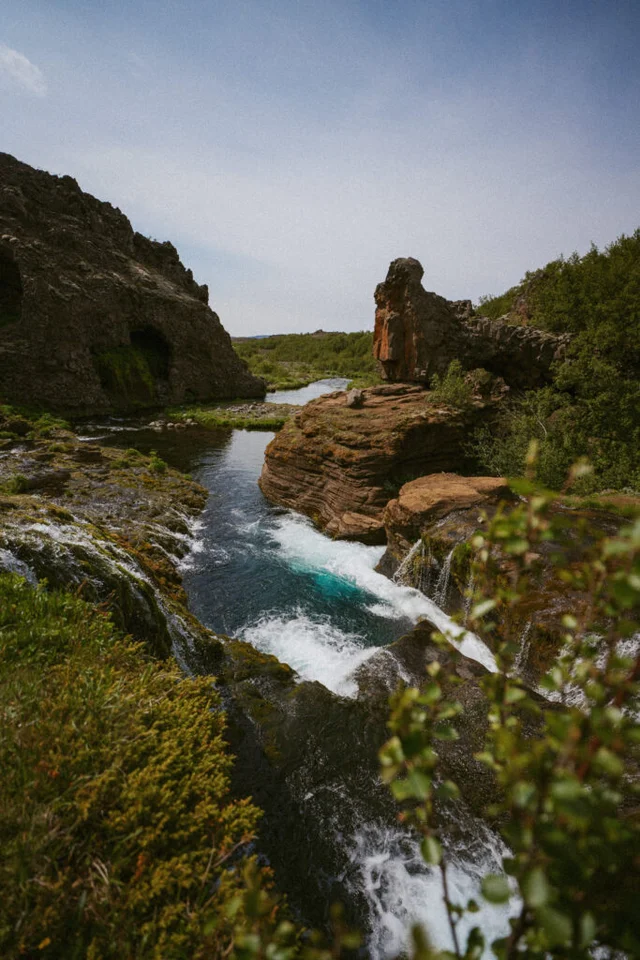 Blue stream running through volcanic rock formations and summer vegetation in Gjáin, Iceland