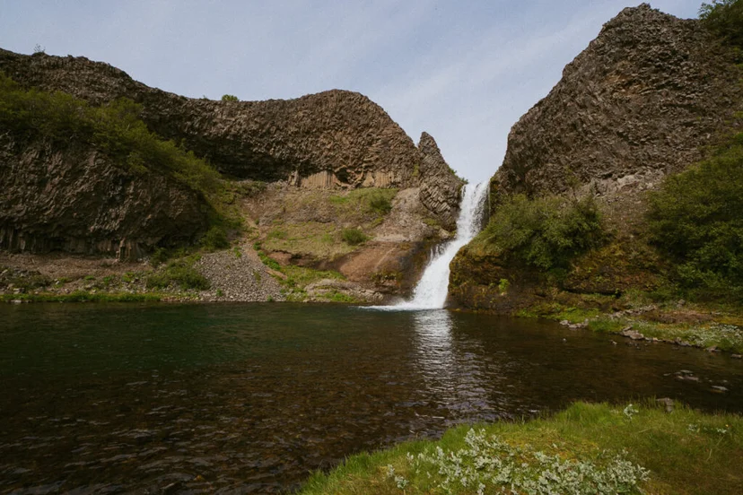 Waterfall flowing into a clear pool surrounded by basalt cliffs at Gjáin valley in Iceland