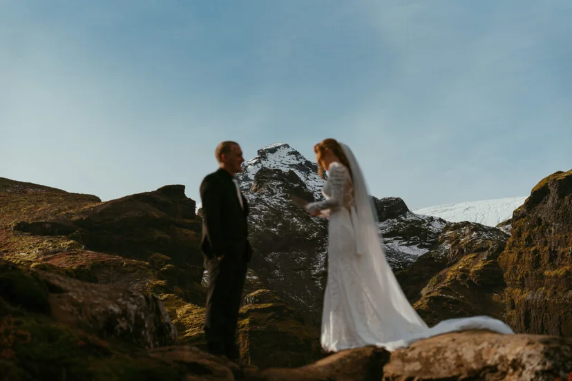 Couple holding hands on a cliff edge in Múlagljúfur Canyon with glacier views in the background