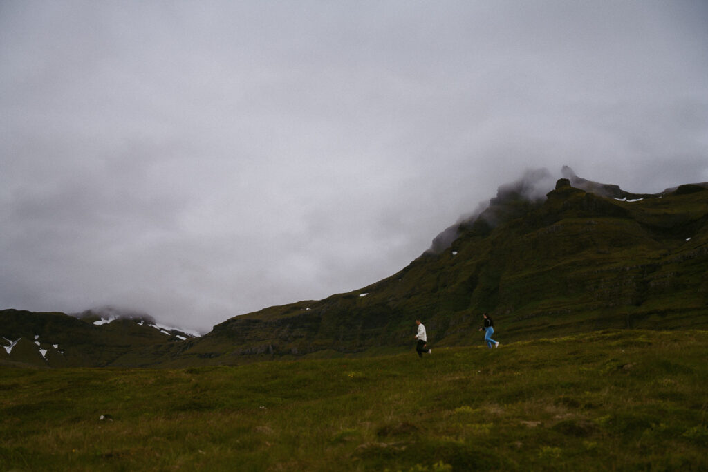 Couple walking through a green field with misty mountains near Kirkjufell in the background