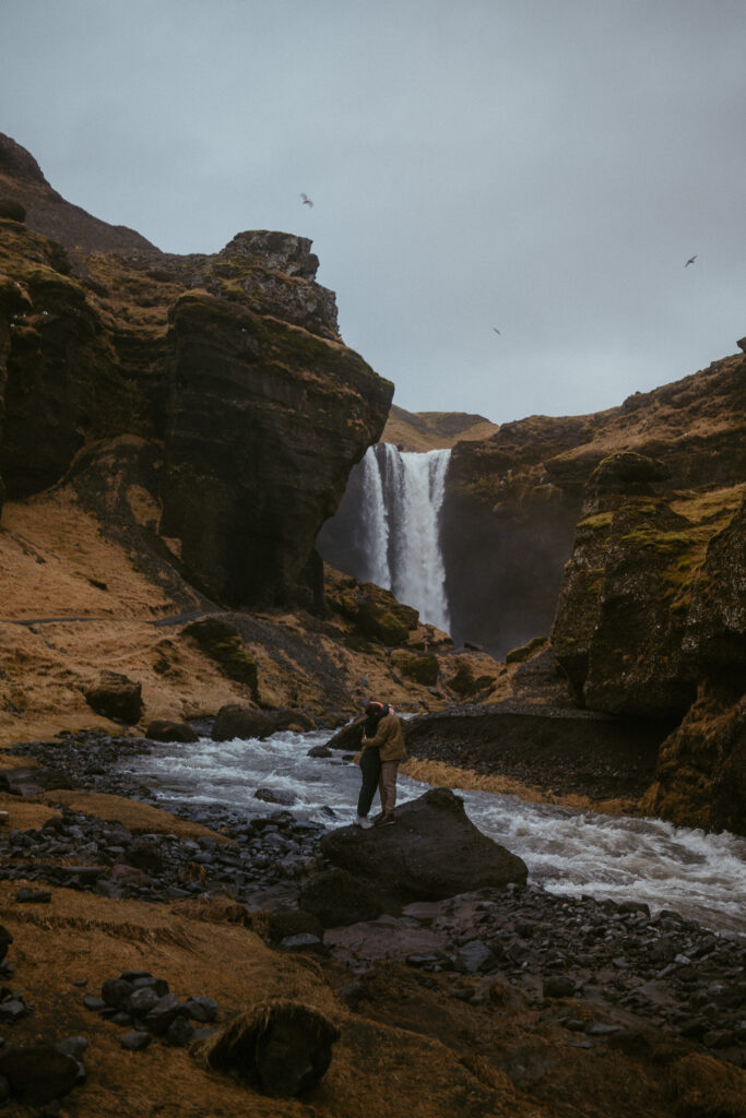 kvernufoss waterfall in iceland in january winter, couple standing on a rock