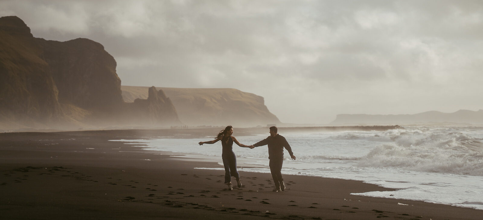 Couple having an engagement session in Icelands black sand beach running on the beach with beautiful light