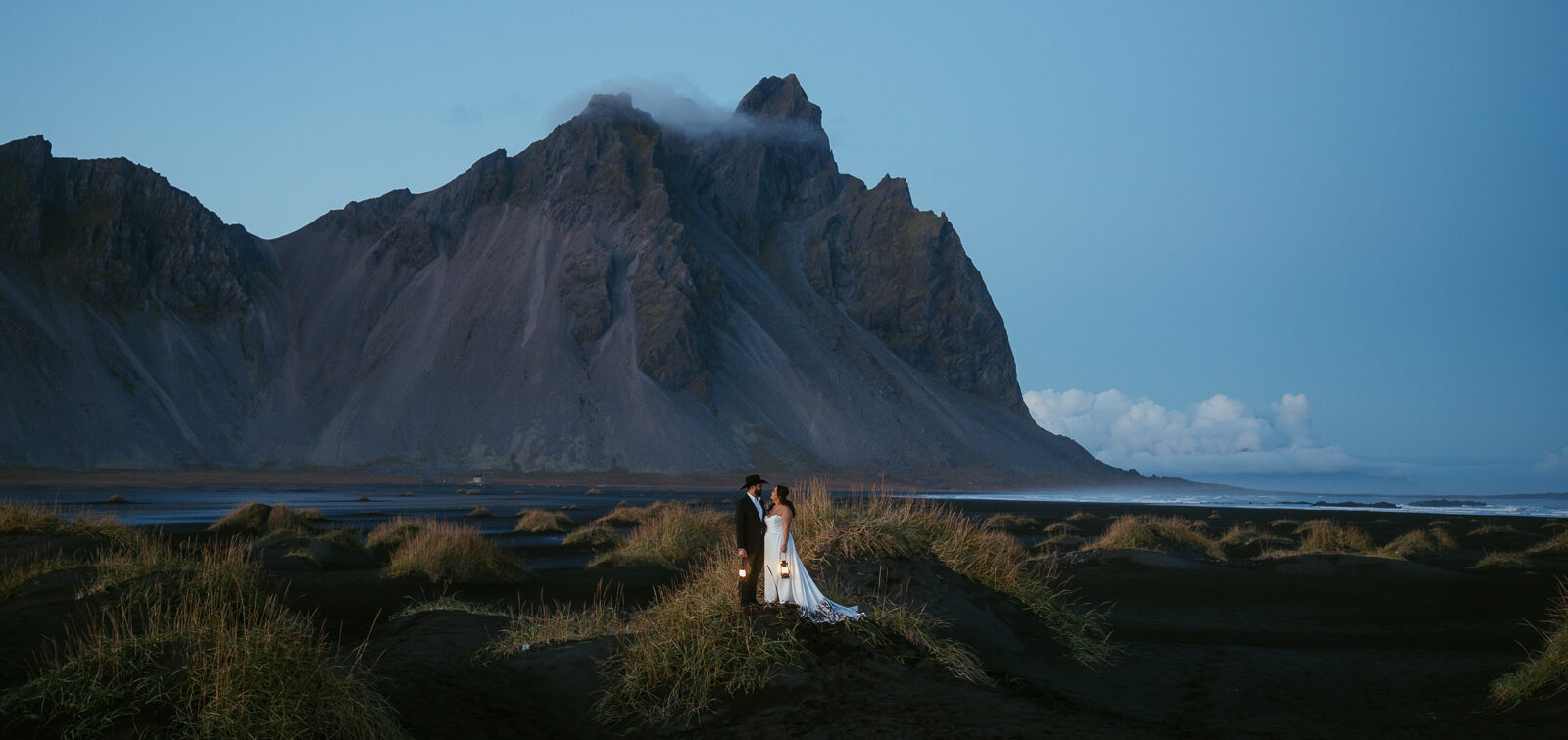A couple from Texas eloping in iceland standing on a black sand dune in front of Vestrahorn mountains holding lanterns