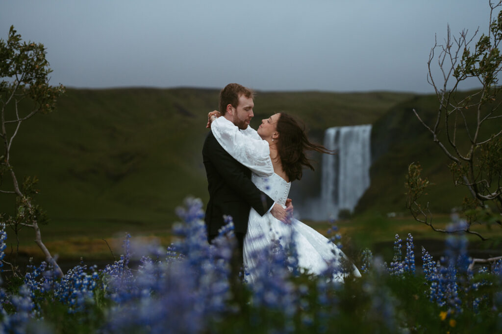 couple in wedding attire running in a lupine field in iceland after eloping