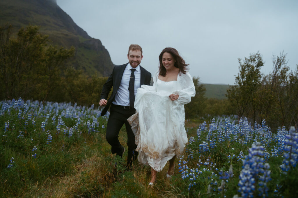 couple in wedding attire running in a lupine field in iceland
