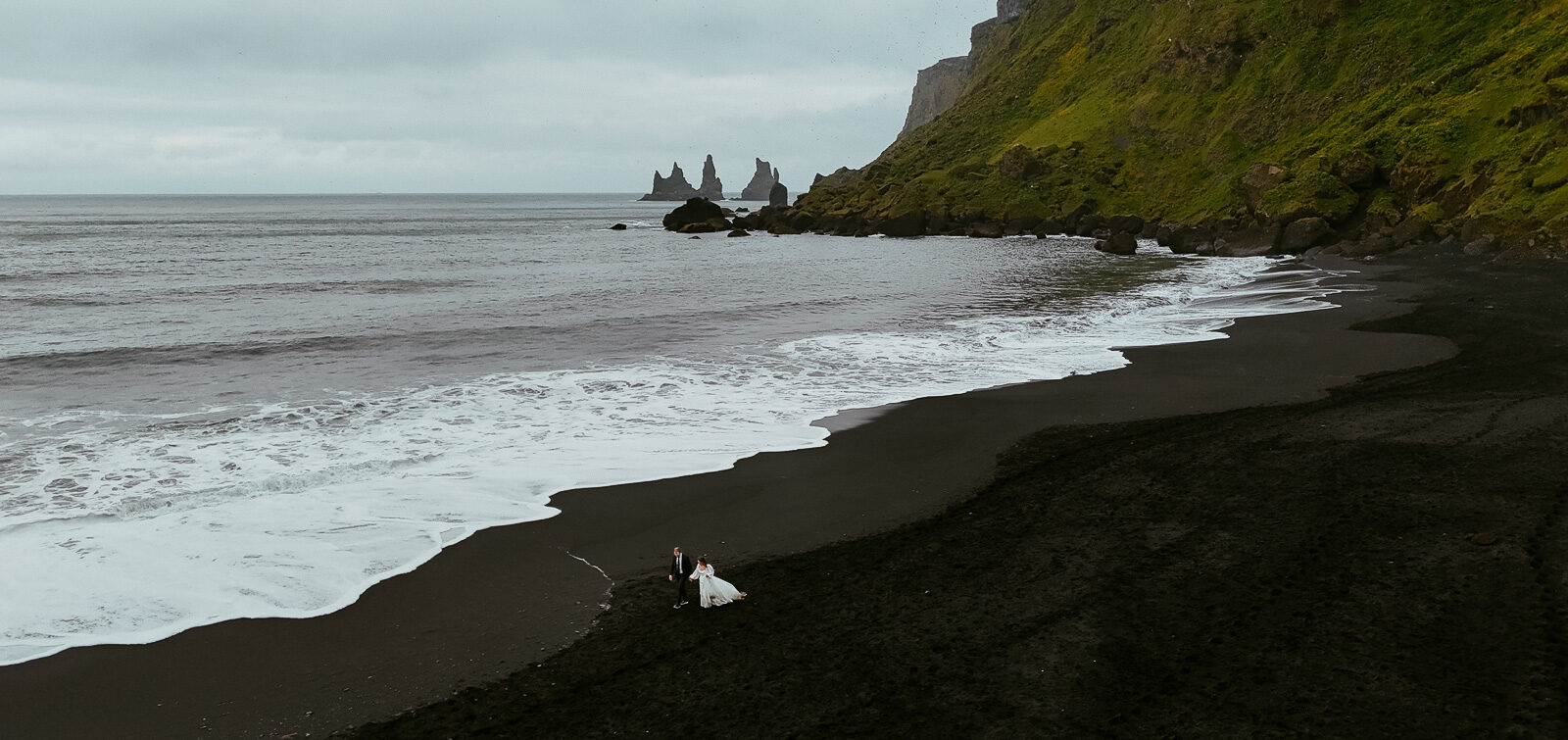 couple who just got married in iceland running on black sand in the beach