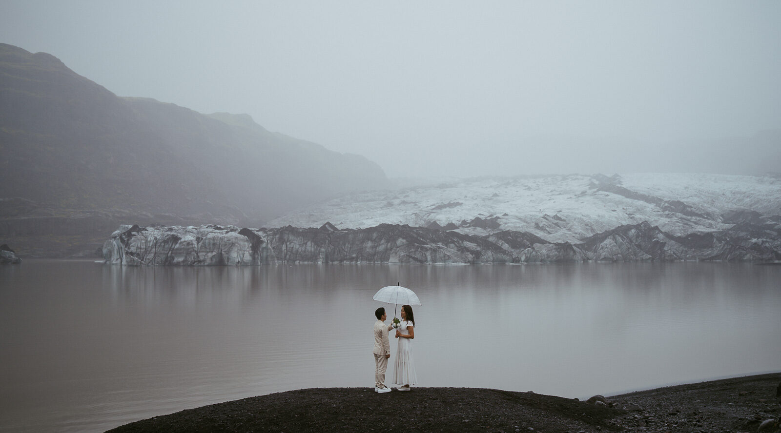 couple eloping in iceland standing in front of a glacier with an umbrella